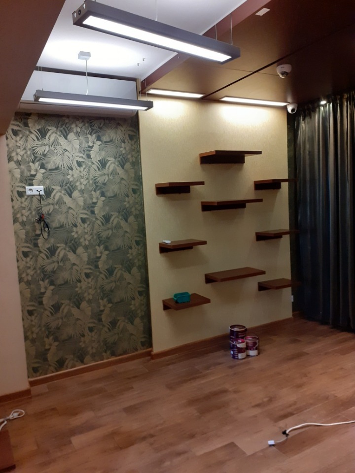 Pokój po remoncie z tapetą w liście i pomalowaną ścianą z półkami, widoczne puszki z farbą na podłodze.