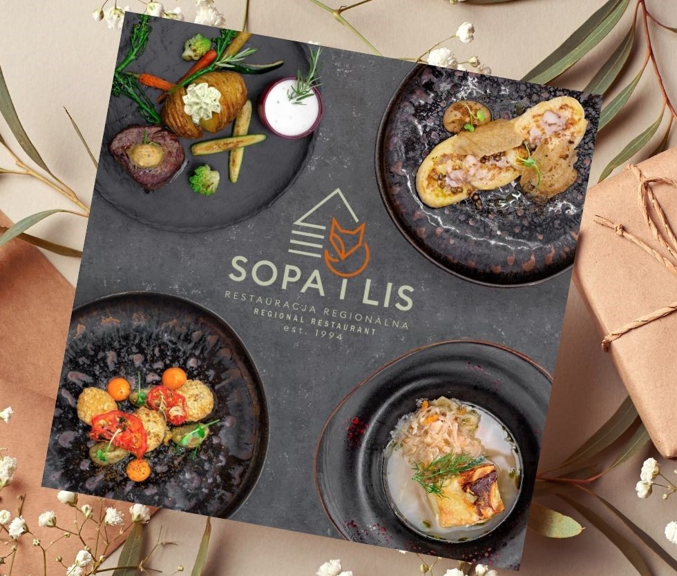 Kwadratowa kompozycja z czterech dań restauracji Sopa i Lis na ciemnych talerzach, otoczona dekoracyjnymi gałązkami i zapakowanym prezentem.