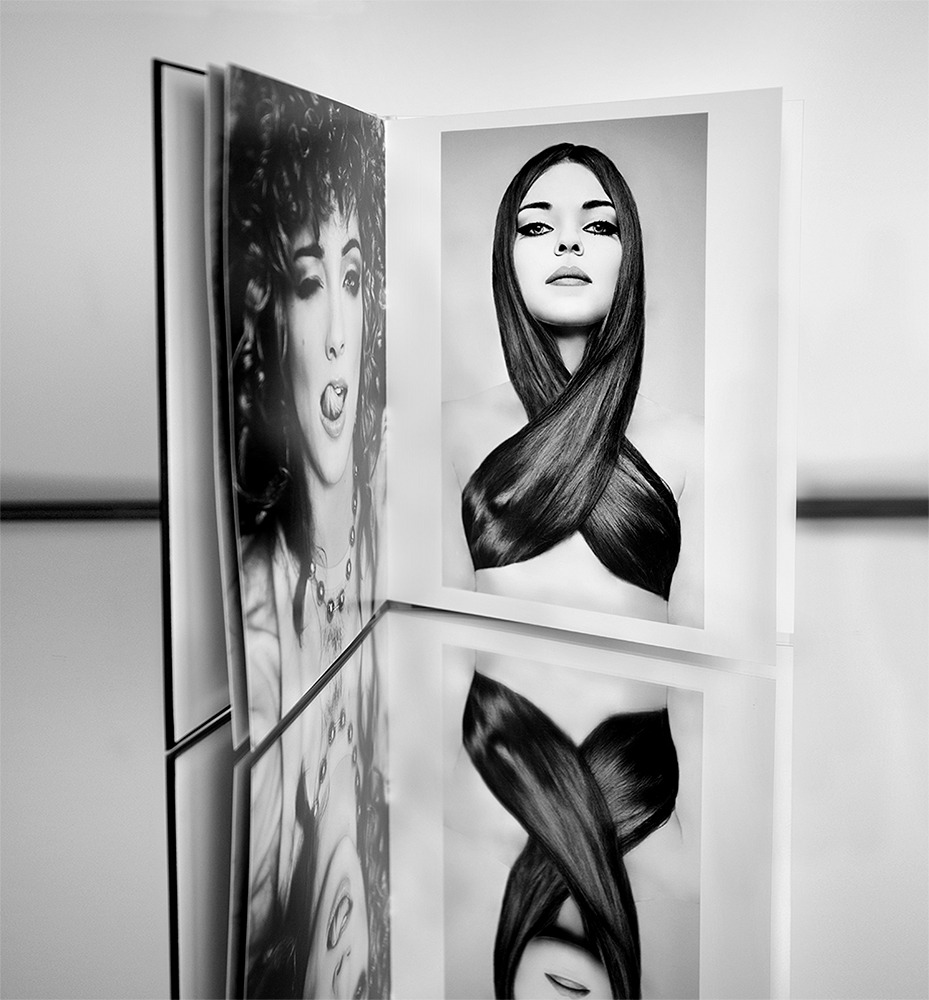 Otwarty album fotograficzny prezentujący czarno-białe portrety kobiet, z odbiciem w błyszczącej powierzchni, ukazujący różnorodność stylów i ekspresji.