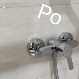 Bateria prysznicowa z chromowanym wykończeniem zamontowana na beżowej ścianie z płytek imitujących marmur, widoczne ślady po czyszczeniu.