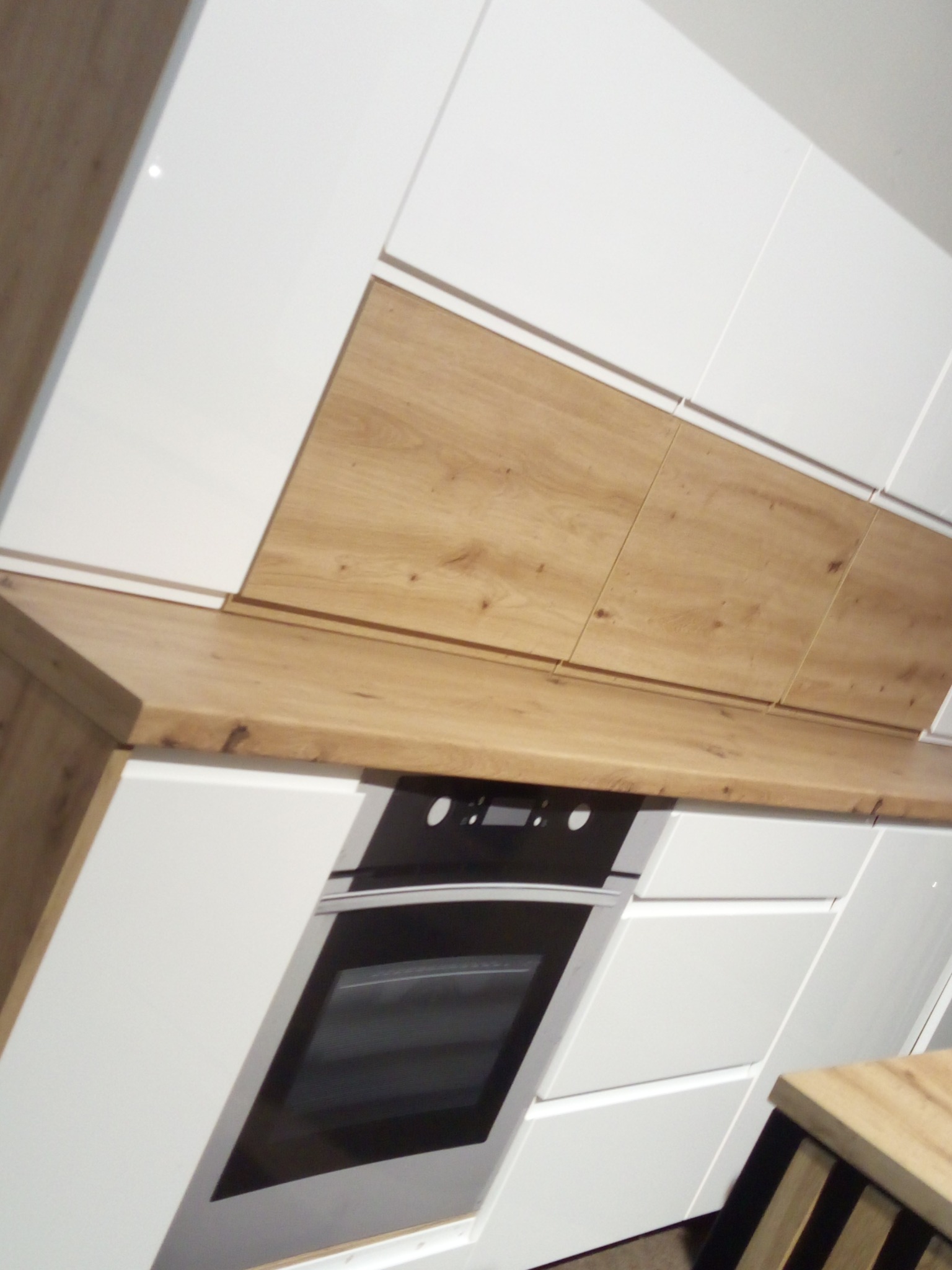 Nowoczesna kuchnia z białymi lakierowanymi frontami i drewnianym blatem. Widoczny piekarnik w zabudowie.