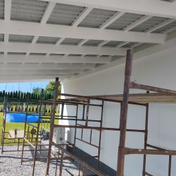 Tartacznictwo Usługi-Produkcja - Montaż zadaszenia tarasu z widocznym stelażem rusztowania i basenem w tle.