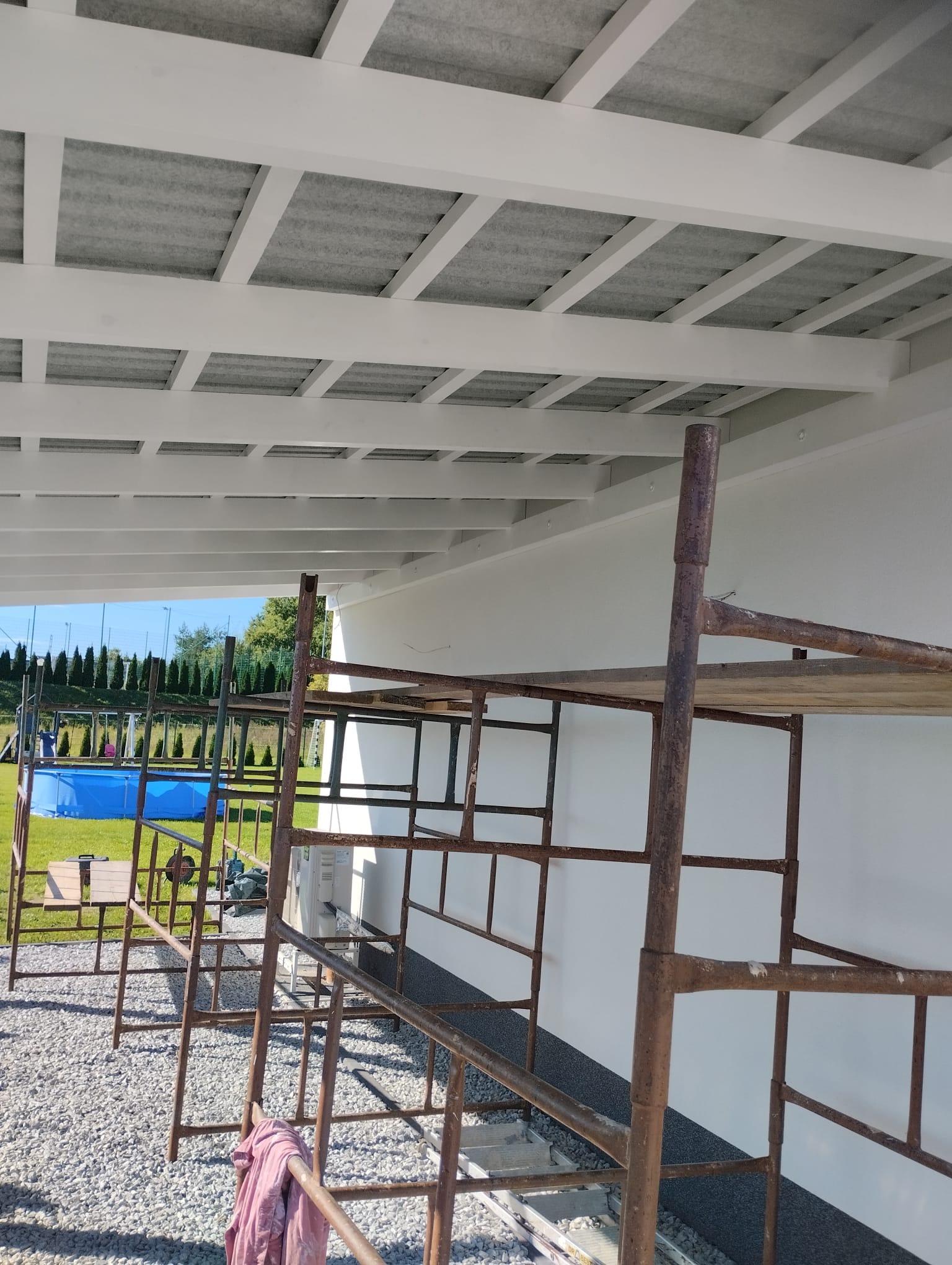 Montaż zadaszenia tarasu z widocznym stelażem rusztowania i basenem w tle.