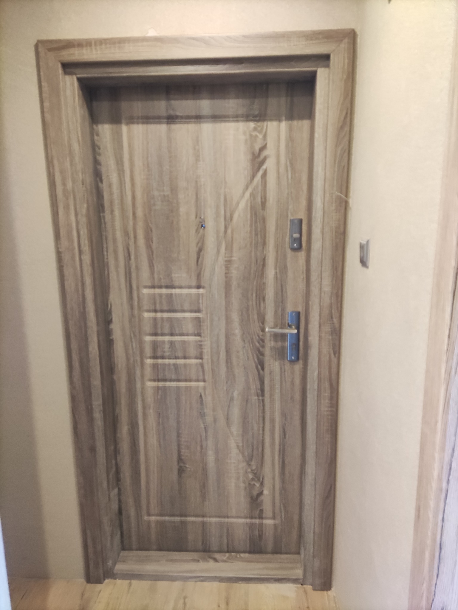 Zamontowane drzwi wejściowe z drewnopodobnym wykończeniem w Pabianicach, widoczne zamek, wizjer i poziome frezy dekoracyjne.