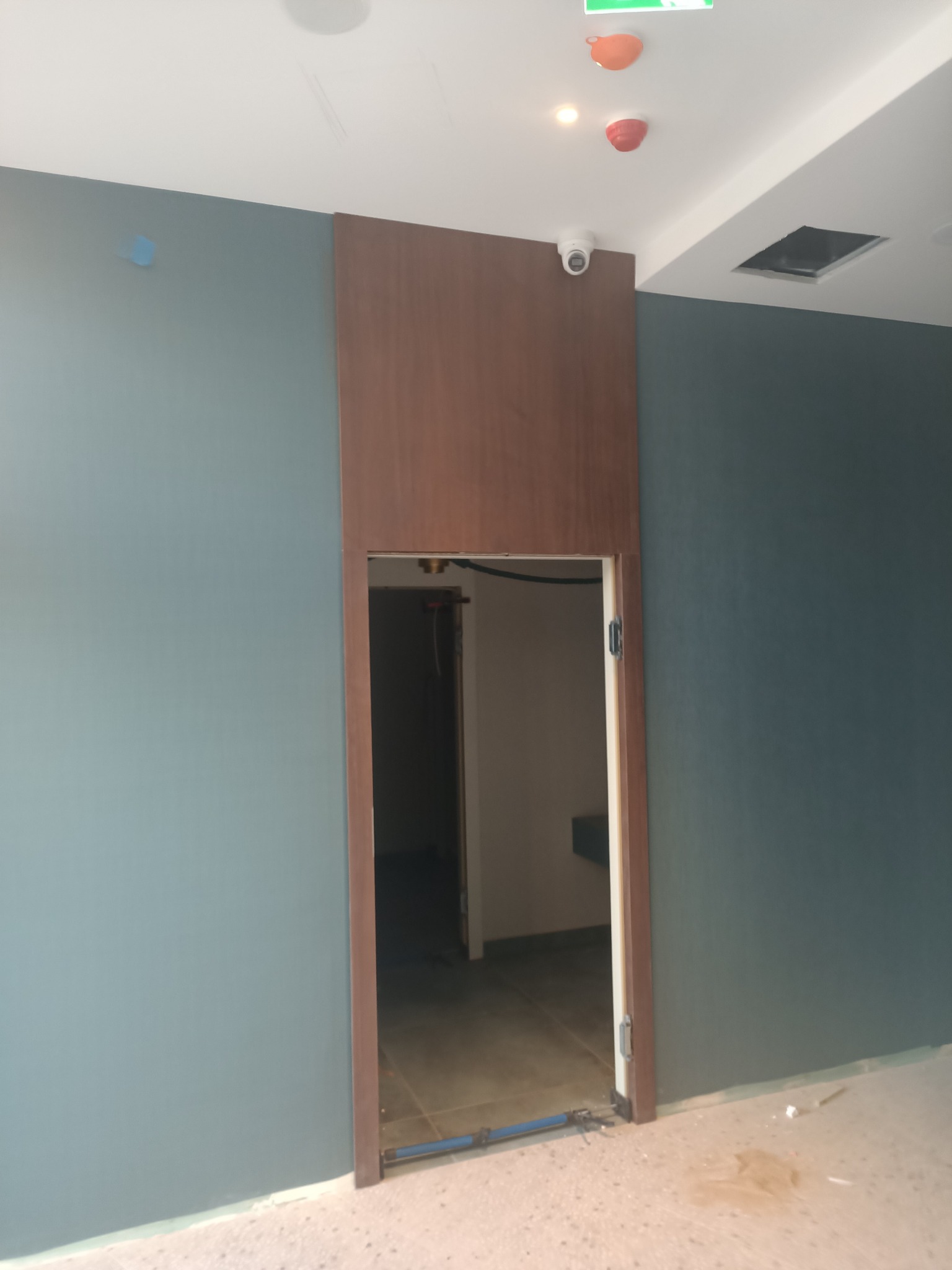 Wnętrze z zamontowanymi drzwiami z ciemnego drewna, widoczna szpachla na podłodze i niebieska rurka do montażu.