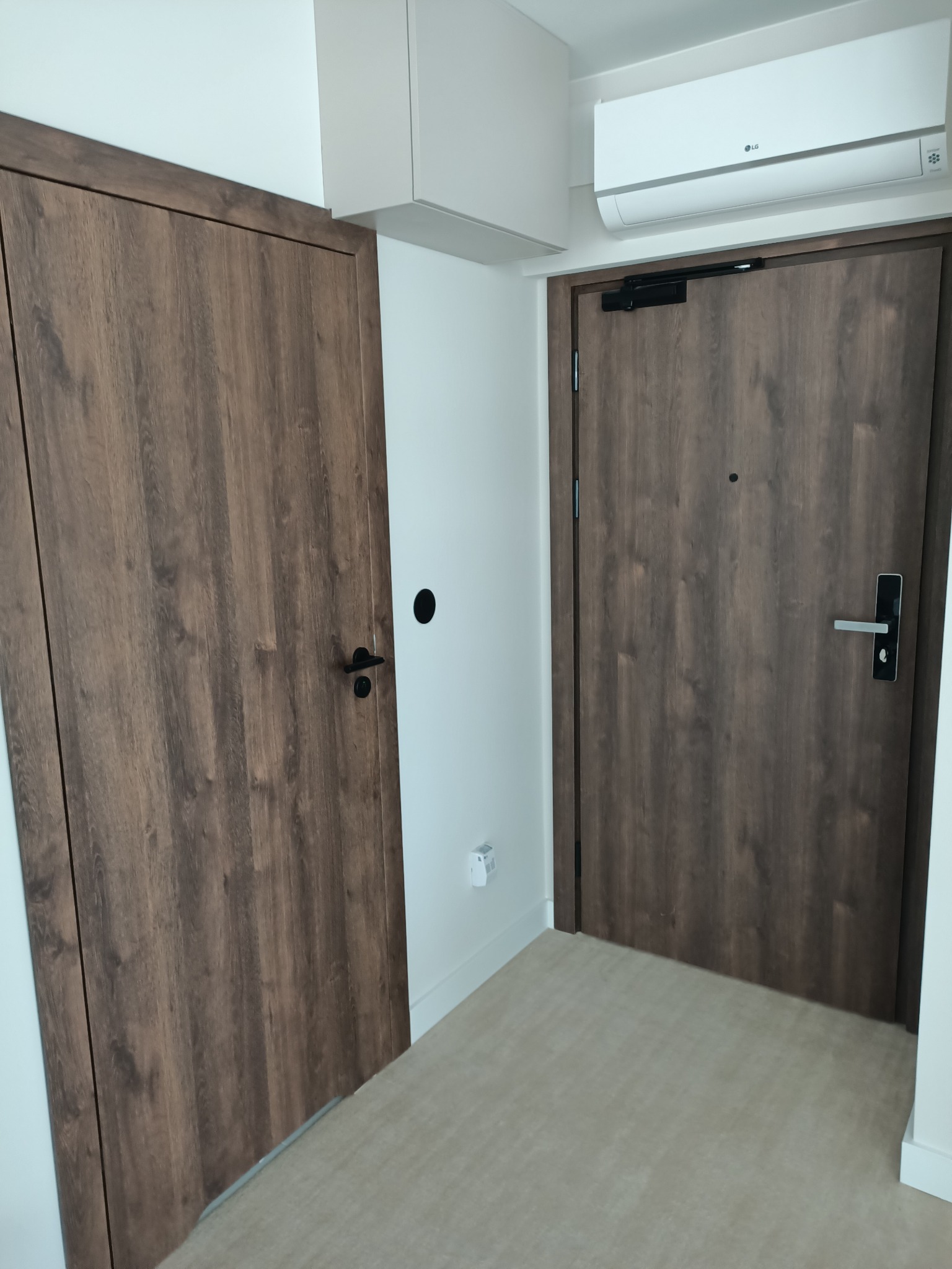 Dwa brązowe drzwi z drewnopodobnym wzorem w nowoczesnym wnętrzu z klimatyzacją na ścianie i jasną podłogą.