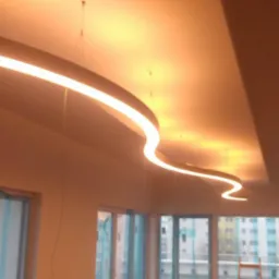 Falista lampa LED zawieszona pod sufitem w nowym pomieszczeniu z widokiem na budynki za oknem.