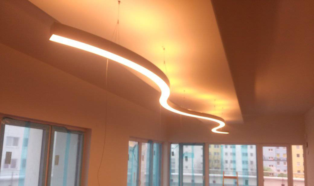 Falista lampa LED zawieszona pod sufitem w nowym pomieszczeniu z widokiem na budynki za oknem.