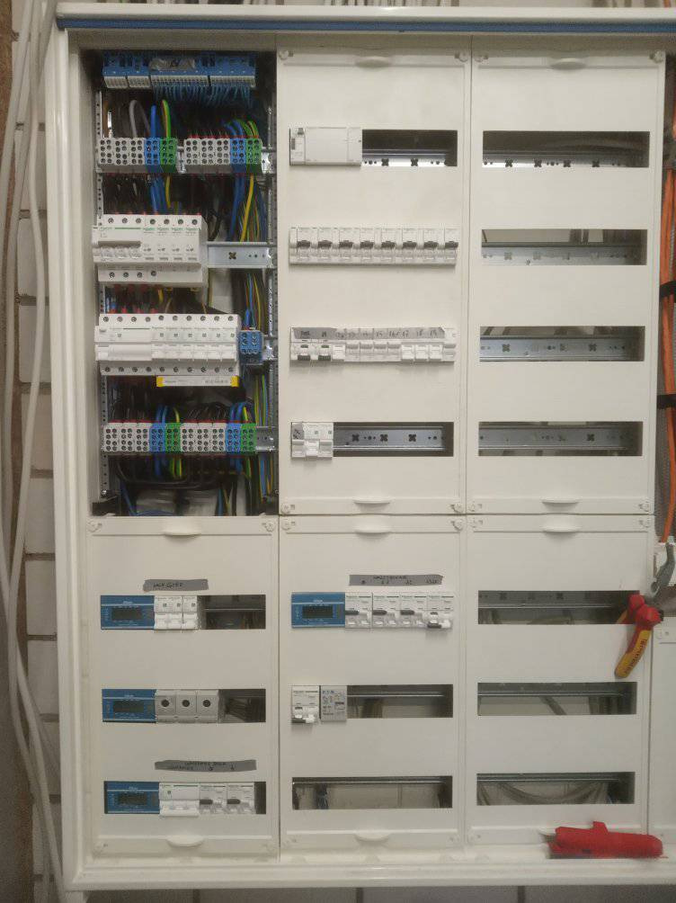 Rozdzielnica elektryczna z widocznymi bezpiecznikami, przewodami i listwami zaciskowymi, częściowo otwarta, z narzędziami obok.