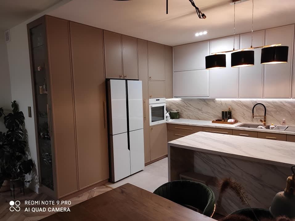 Nowoczesna kuchnia z beżowymi szafkami, białymi frontami, wyspą z marmurowym blatem i czarnymi lampami wiszącymi.