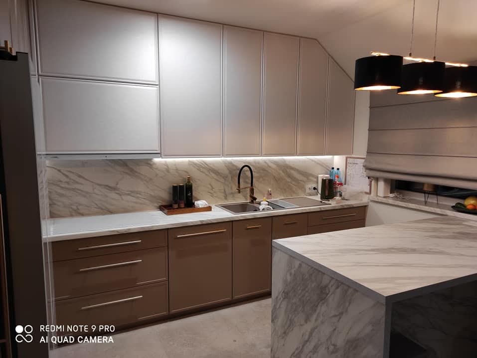 Nowoczesna kuchnia z białymi górnymi szafkami i brązowymi dolnymi szafkami, marmurowym blatem i wyspą, oświetleniem LED pod szafkami wiszącymi i czarnymi lampami wiszącymi