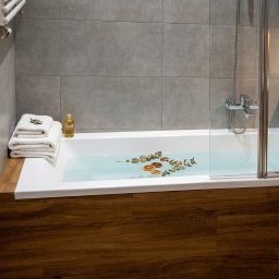AMGREM SMART BUILDING SOLUTIONS ANATOLII GLADYSH - Nowoczesna łazienka z wanną obudowaną drewnem, szklanym parawanem i szarymi płytkami. Na wannie dekoracje z suszonych owoców i liści. Minimalistyczny design.