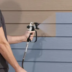 Malowanie desek elewacyjnych pistoletem natryskowym, widoczna różnica kolorów między starą a nową farbą.