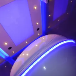 Wnętrze kabiny floatingowej z podświetleniem LED, widok z dołu na białą kapsułę i sufit z lampami punktowymi i podświetleniem w kolorze niebieskim.