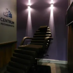 Wnętrze gabinetu z fotelem do terapii, oświetlonym punktowymi lampami na fioletowej ścianie, obok logo Centrum Psychosomatyki.