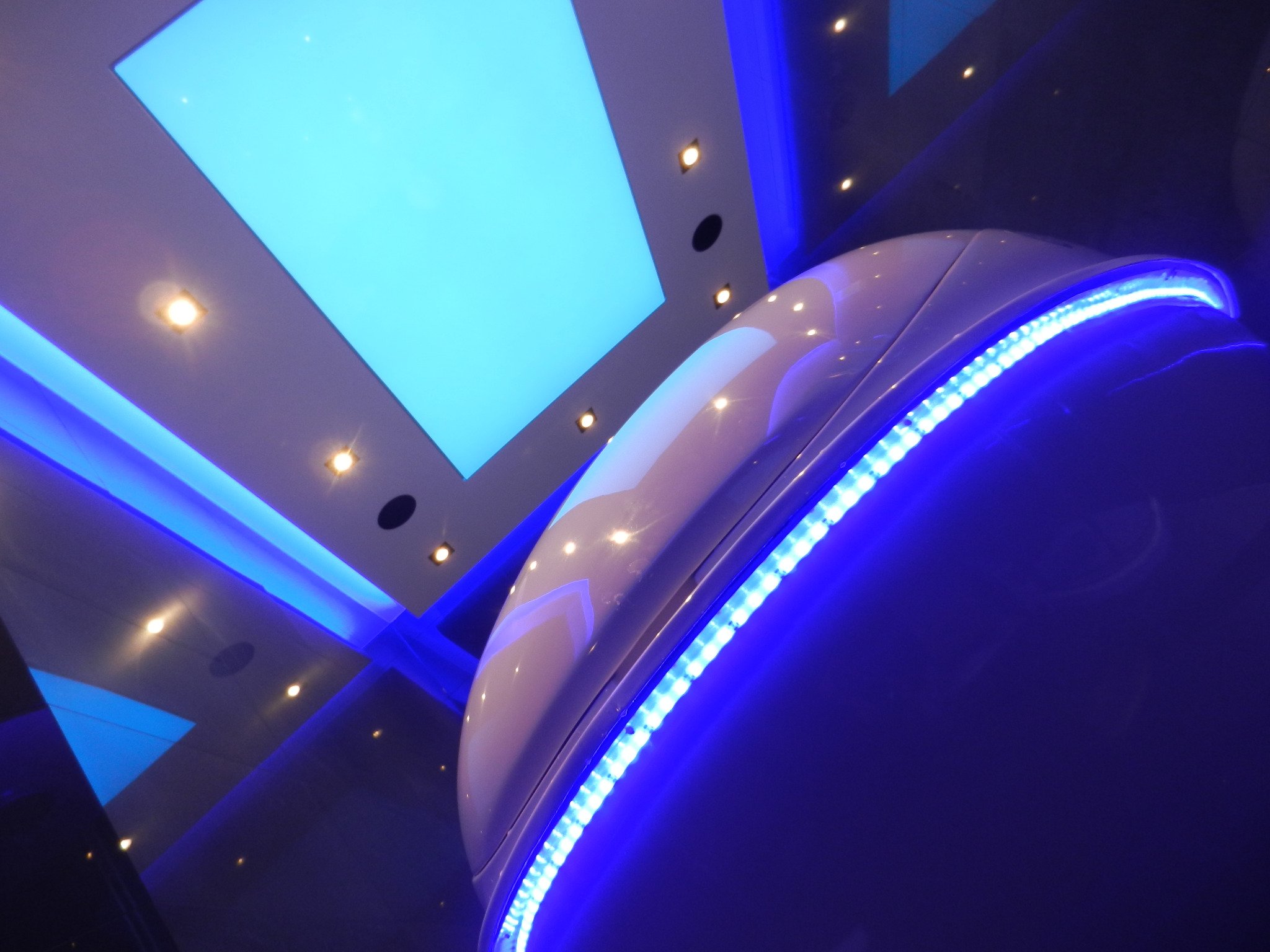 Nowoczesna kapsuła relaksacyjna z niebieskim oświetleniem LED w pomieszczeniu z designerskim sufitem i punktowymi lampami.