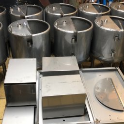 Piotr witkowski - Partia cylindrycznych zbiorników ze stali nierdzewnej z elementami prostokątnymi, przygotowanych do dalszego montażu lub dystrybucji, widoczne spawy i otwory montażowe.