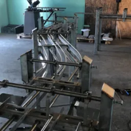 Metalowa konstrukcja w warsztacie, prawdopodobnie element linii produkcyjnej, z widocznymi spawami i elementami montażowymi, w tle maszyna do obróbki metalu.