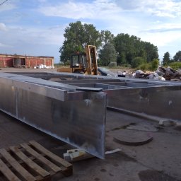 Piotr witkowski - Metalowa konstrukcja szkieletowa, prawdopodobnie pod budowę hali, widoczna na zewnątrz, z wózkiem widłowym w tle i elementami rusztowania, sugerująca etap montażu lub przygotowania do transportu.