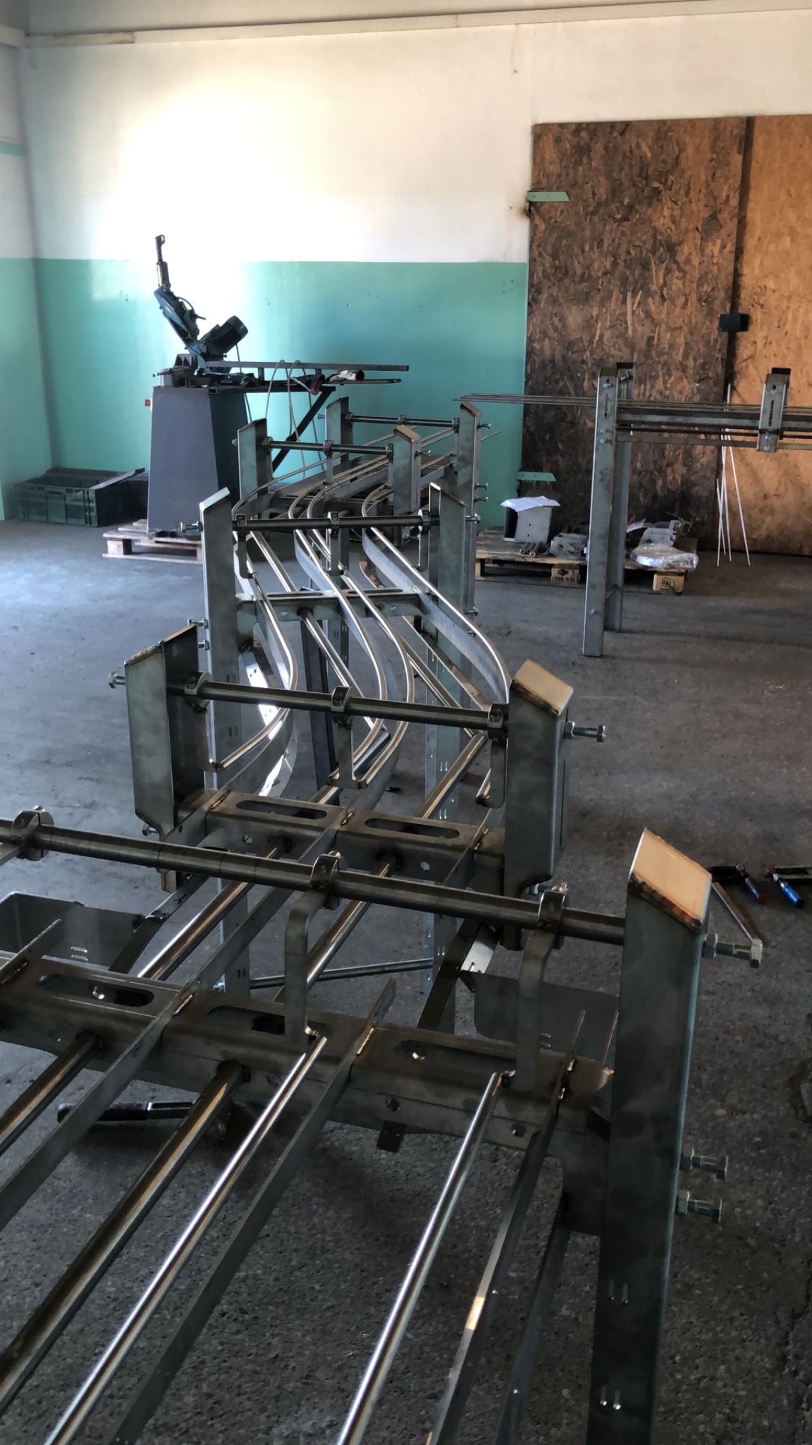 Metalowa konstrukcja w warsztacie, prawdopodobnie element linii produkcyjnej, z widocznymi spawami i elementami montażowymi, w tle maszyna do obróbki metalu.