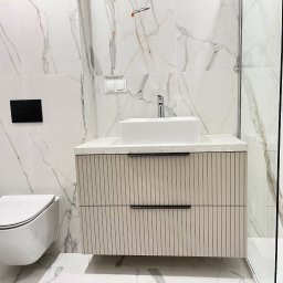 ROJANI SPÓŁKA Z OGRANICZONĄ ODPOWIEDZIALNOŚCIĄ - Nowoczesna łazienka z marmurowymi płytkami, wiszącą toaletą i szafką pod umywalkę z ryflowanymi frontami. Minimalistyczny design, chromowana armatura.