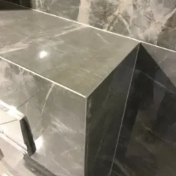 Szare marmurowe płytki ułożone na półce i ścianie w łazience, widoczne fugi i narożnik.