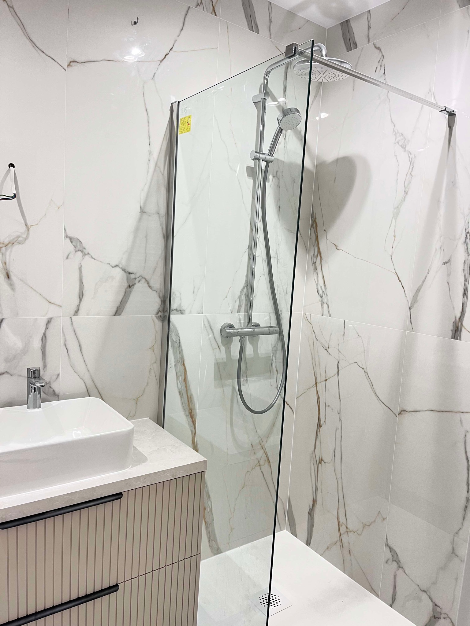 Nowoczesna łazienka z kabiną prysznicową typu walk-in, białą umywalką nablatową i marmurowymi płytkami. Minimalistyczny design, chromowana armatura, eleganckie wykończenie.