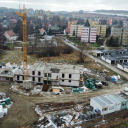 OstBudHousDom - Budowa dwukondygnacyjnego budynku z pustaków, widok z góry. Na pierwszym planie składowane materiały budowlane, w tle zabudowa miejska i dźwig budowlany.