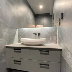 Nowoczesna łazienka w odcieniach szarości z owalną umywalką nablatową, minimalistyczną armaturą i lustrem optycznie powiększającym przestrzeń.