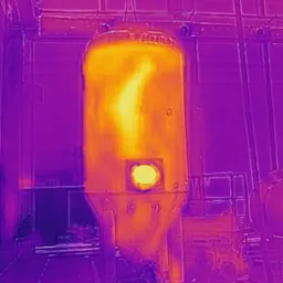 Termowizyjne zdjęcie cylindrycznego zbiornika podwieszonego na haku, z widocznym rozkładem temperatur i miejscem o podwyższonej temperaturze na ścianie bocznej.