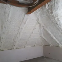 Poddasze po natrysku pianki izolacyjnej, widoczne krokwie i fragment instalacji elektrycznej. Ściany częściowo wykończone płytami gipsowo-kartonowymi.