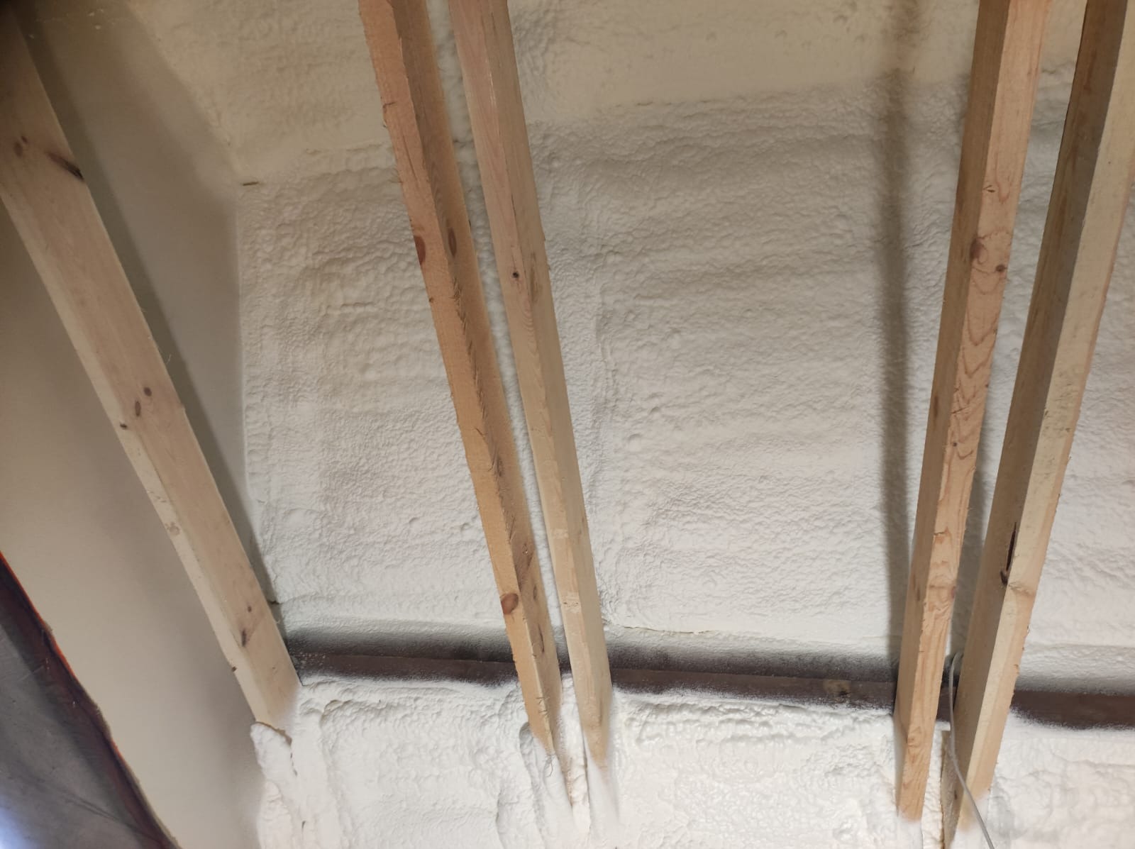 Poddasze po ociepleniu pianką PUR, widoczne drewniane krokwie i równomierna warstwa izolacji w kolorze białym. Detal wykończenia izolacji.
