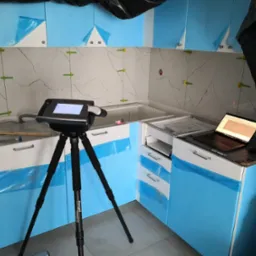 Montaż płytek imitujących marmur na ścianie kuchni, z użyciem krzyżyków dystansowych; widoczny skaner 3D na statywie oraz laptop na blacie roboczym.