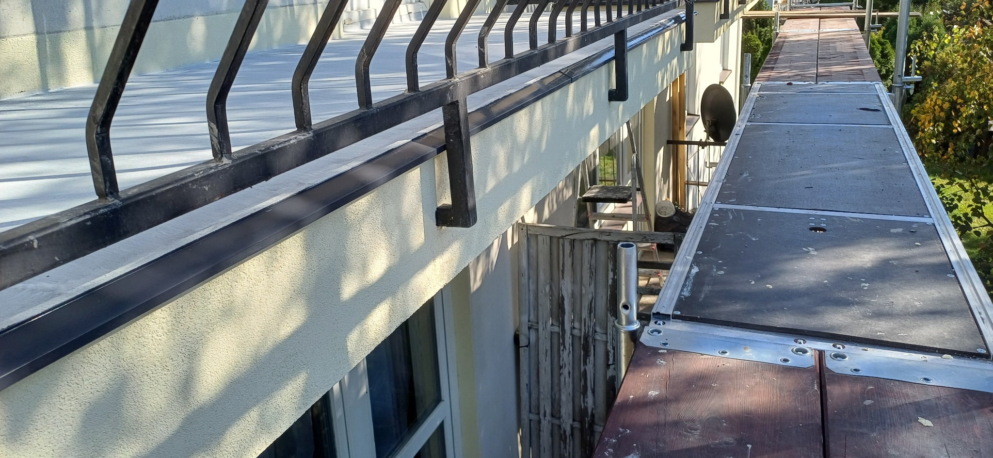 Ocieplona elewacja budynku z czarną barierką balkonu, widok z rusztowania z drewnianym podestem.