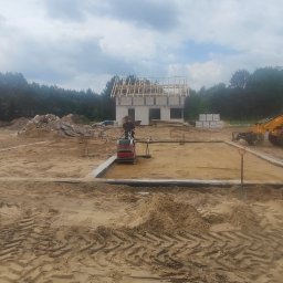 RavBud - Prace ziemne pod fundamenty domu w Międzyzdrojach, widoczny wykop, szalunek, ubijarka i koparko-ładowarka JCB.