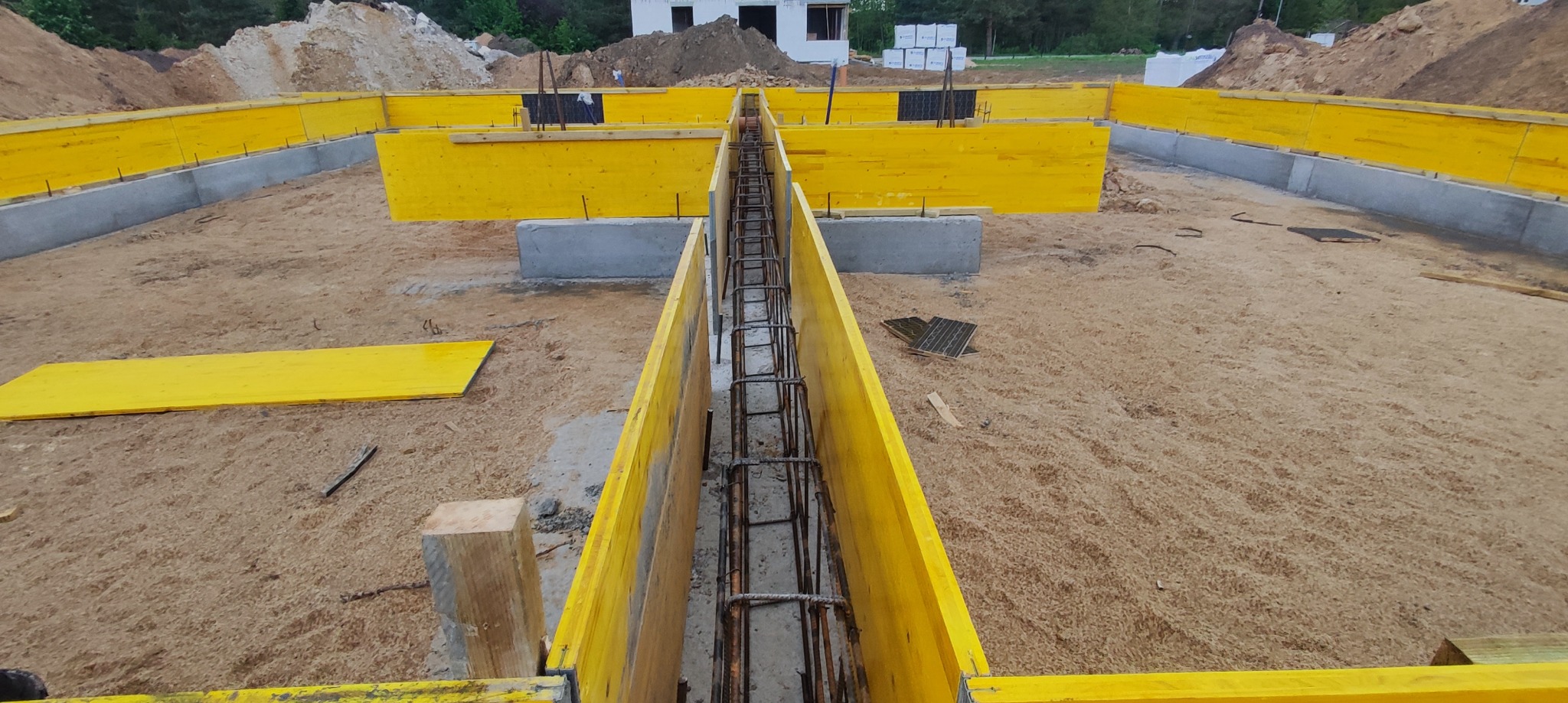 Przygotowanie zbrojenia w wykopie pod fundament, z użyciem żółtych szalunków, widok z góry.