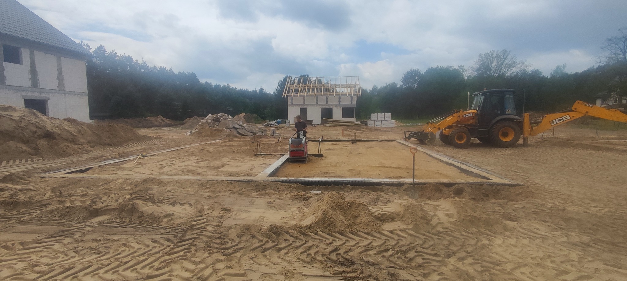 Prace ziemne pod fundamenty domu w Międzyzdrojach, widoczny wykop, szalunek, ubijarka i koparko-ładowarka JCB.