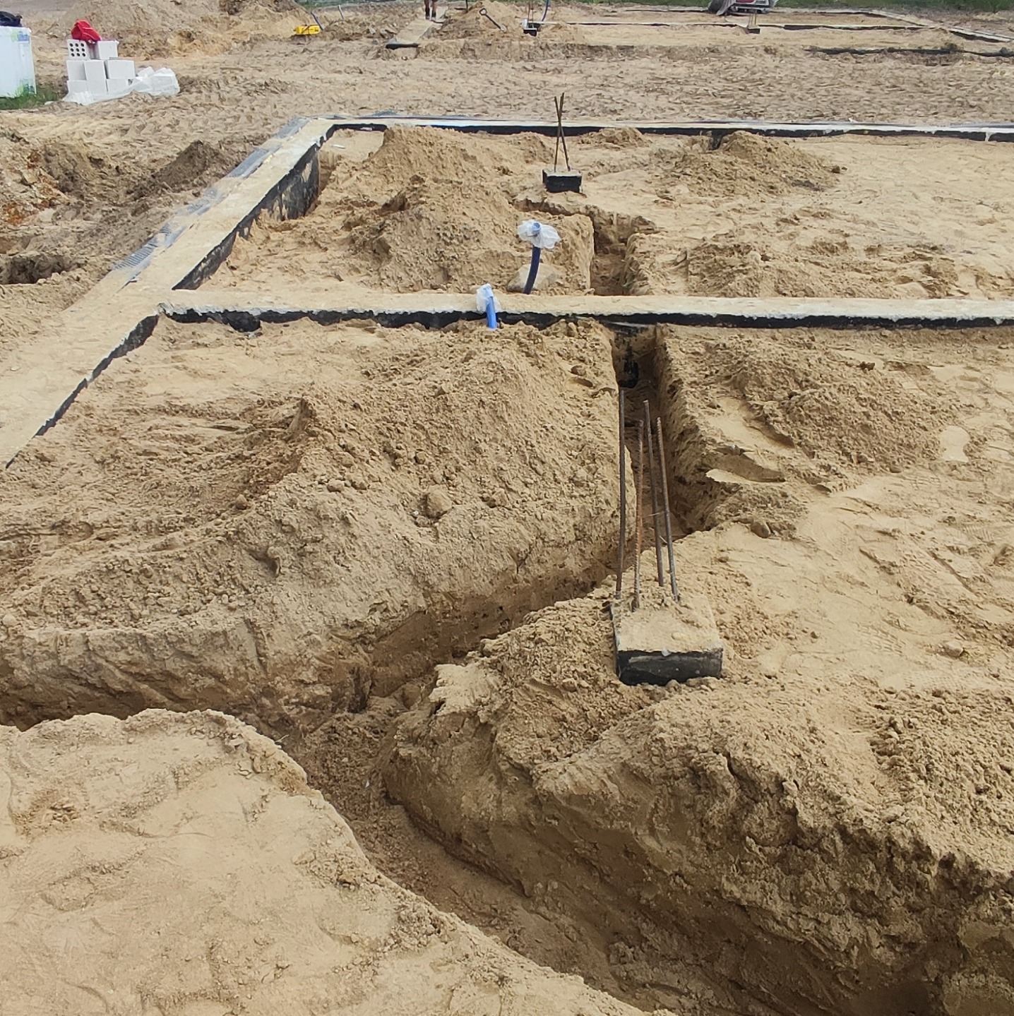 Przygotowanie terenu pod fundamenty: wykopane rowy, zbrojenie wystające z ziemi, izolacja przeciwwilgociowa ułożona w wykopach.