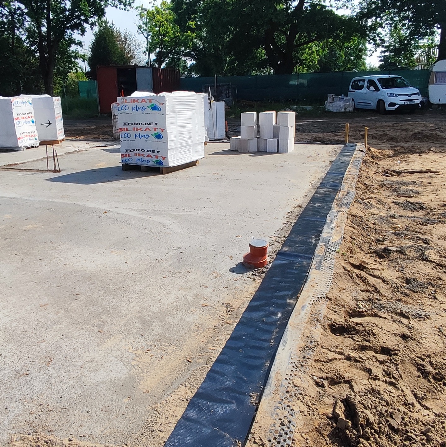 Przygotowany fundament pod budowę z widocznymi paletami z bloczkami silikatowymi, zabezpieczoną folią hydroizolacyjną i wystającą rurą kanalizacyjną.