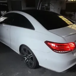 Białe coupe z czarnym dachem, widok z tyłu, lampy tylne włączone, felgi aluminiowe, garażowe otoczenie.