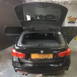 Czarne BMW 320d kombi z otwartą klapą bagażnika i tylnymi drzwiami, widoczne przyciemnione szyby boczne i tylna