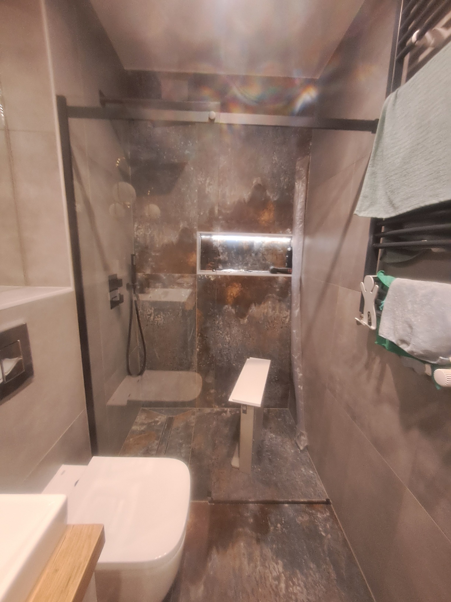 Nowoczesna łazienka z kabiną prysznicową typu walk-in, wykończona płytkami imitującymi rdzę, z podświetlaną niszą i minimalistycznym siedziskiem prysznicowym.