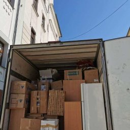 Greg-Trans Grzegorz Śliwa - Wnętrze furgonetki wypełnione kartonami, meblami i lodówką podczas dnia przeprowadzki, z widocznym fragmentem budynku w tle.