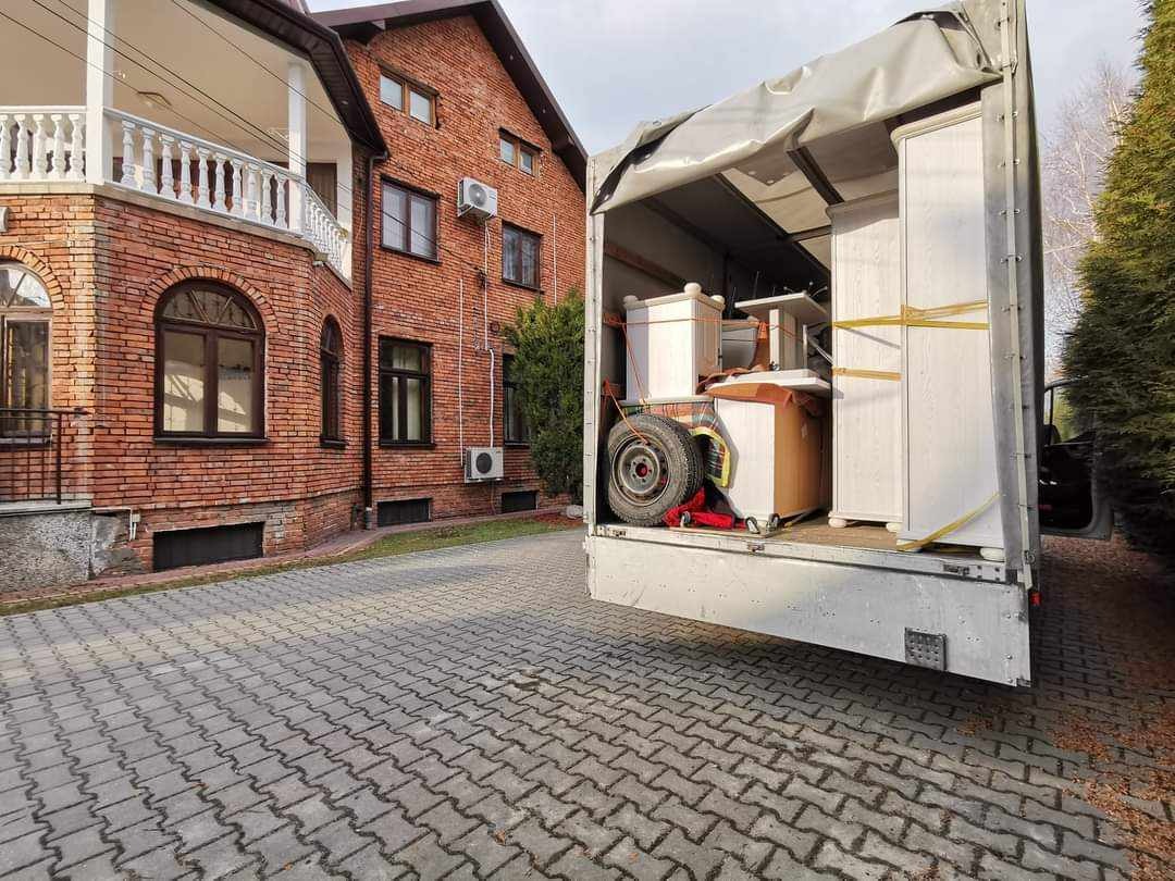 Meble zabezpieczone pasami w przestrzeni ładunkowej busa podczas załadunku przed budynkiem mieszkalnym z cegły.