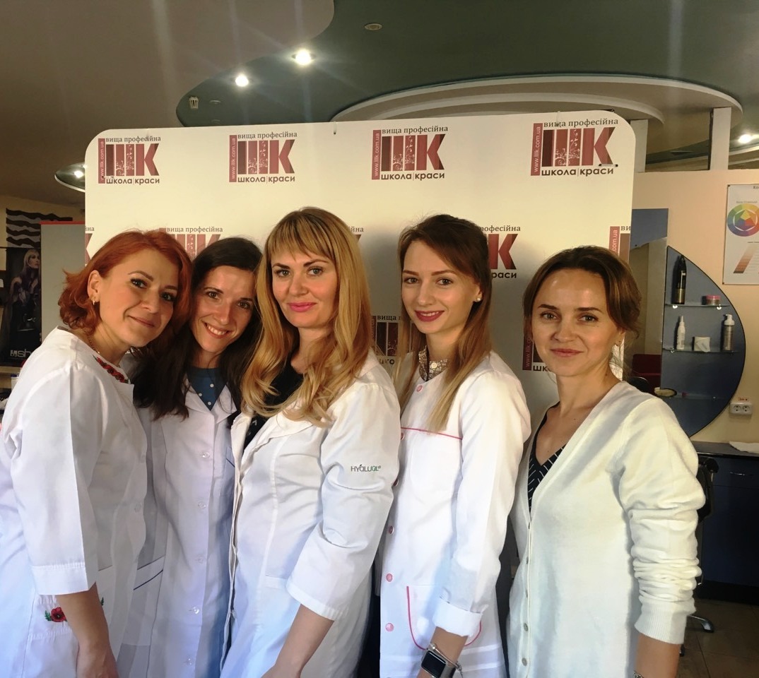 Zespół salonu kosmetycznego w Jedliczach prezentuje się na tle logotypu szkoły kosmetycznej, ubrane w białe uniformy, z uśmiechem.