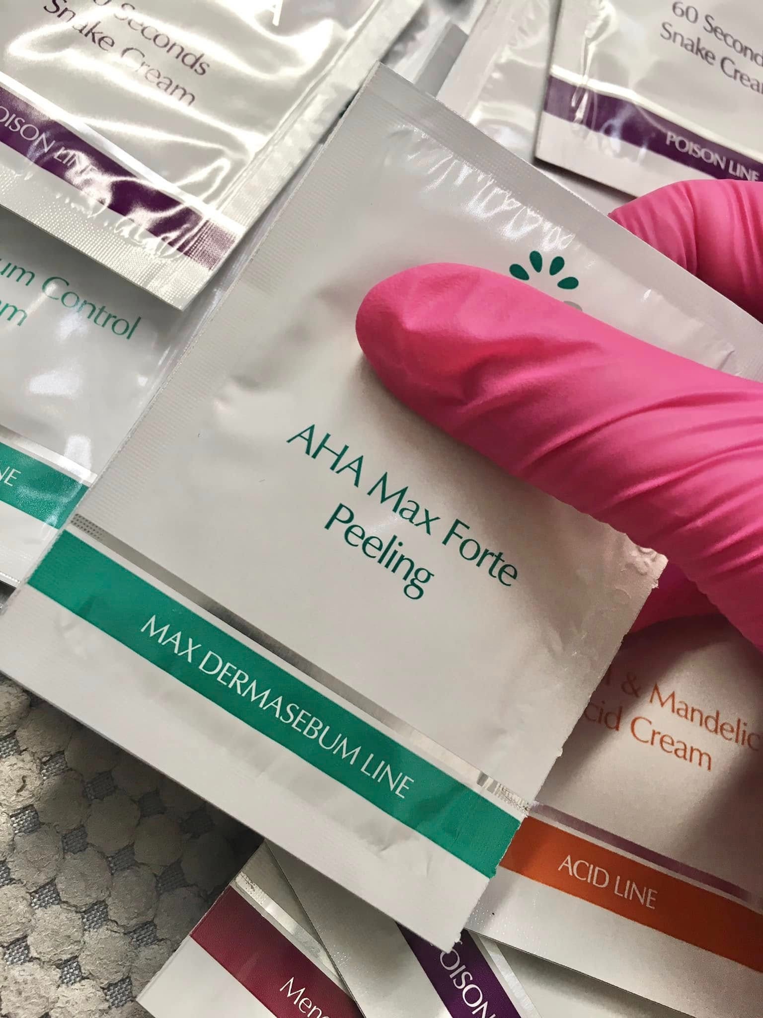 Saszetki z peelingiem AHA Max Forte i innymi kosmetykami, trzymane w dłoni w różowej rękawiczce, gotowe do użycia w salonie kosmetycznym.