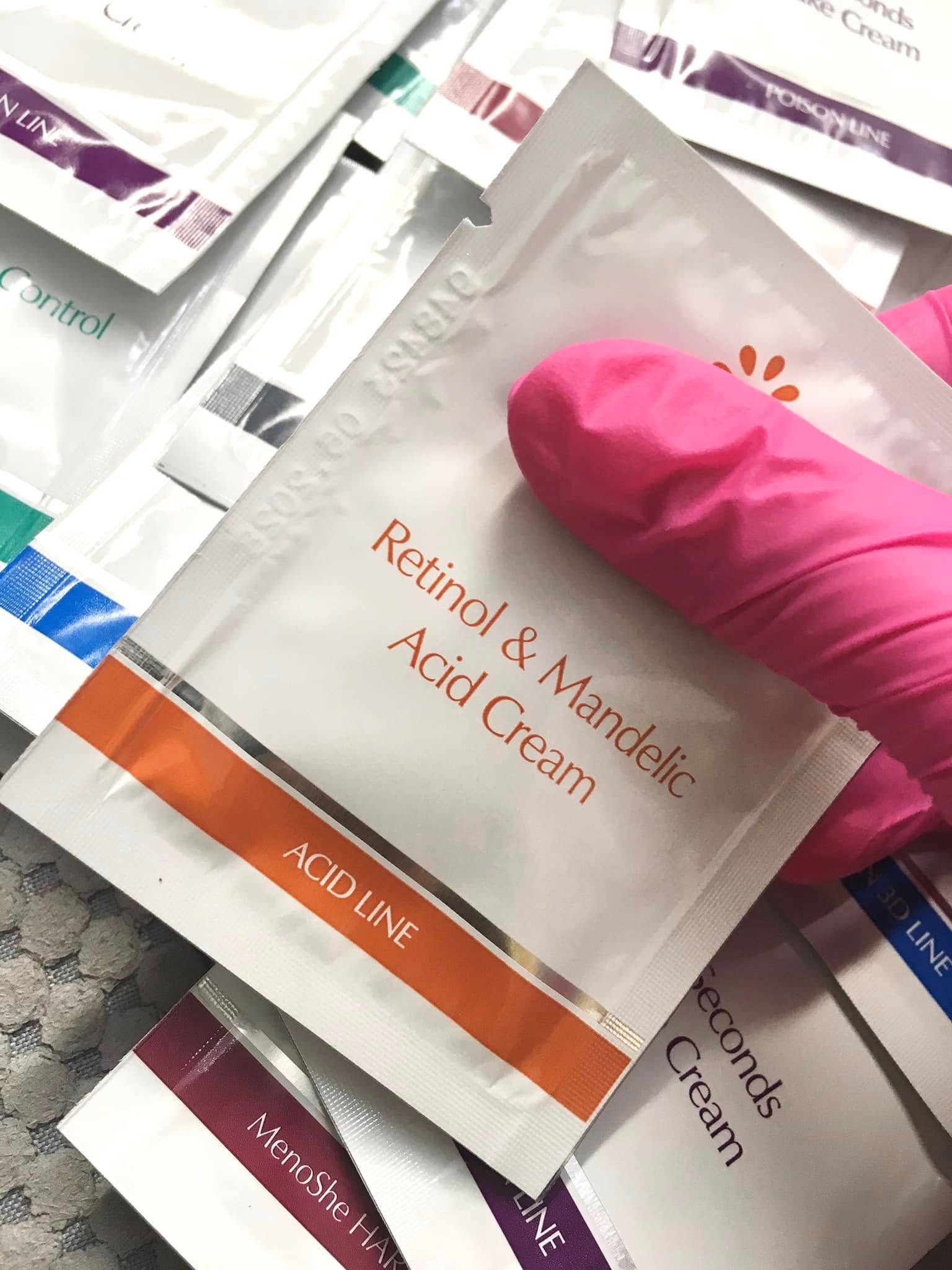 Próbki kremów z retinolem i kwasem migdałowym w dłoni w różowej rękawiczce. Widoczne nazwy serii: Acid Line, Poison Line, MenoShe Hair Line, Control, Seconds Cream.