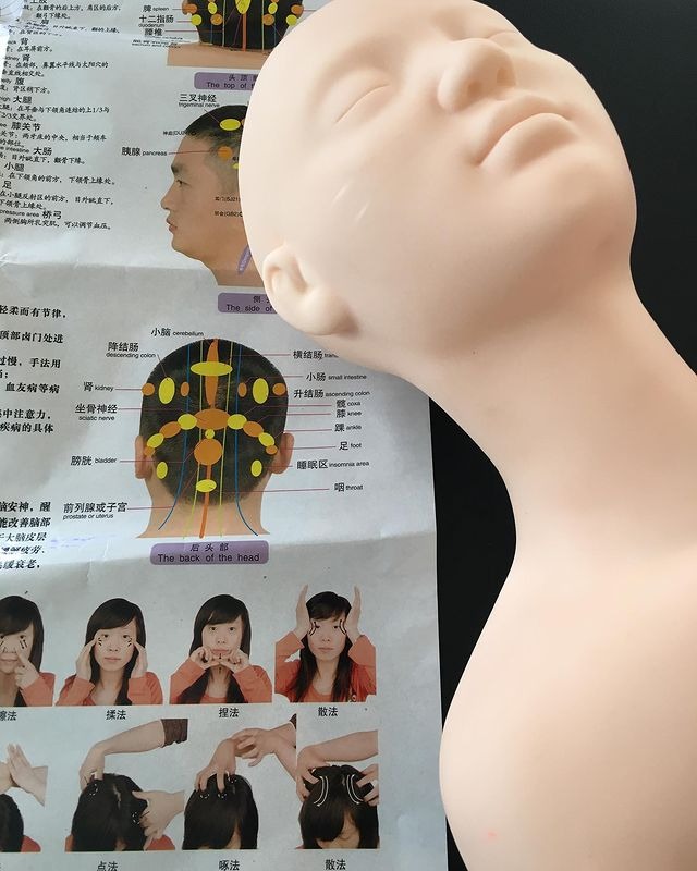 Manekin głowy z zaznaczonymi punktami akupunkturowymi oraz schematami masażu twarzy i głowy w języku chińskim