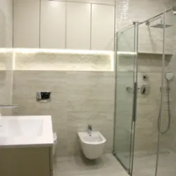 Nowoczesna łazienka w beżowych odcieniach z kabiną prysznicową typu walk-in, podświetlanym blatem z umywalką i bidetem.