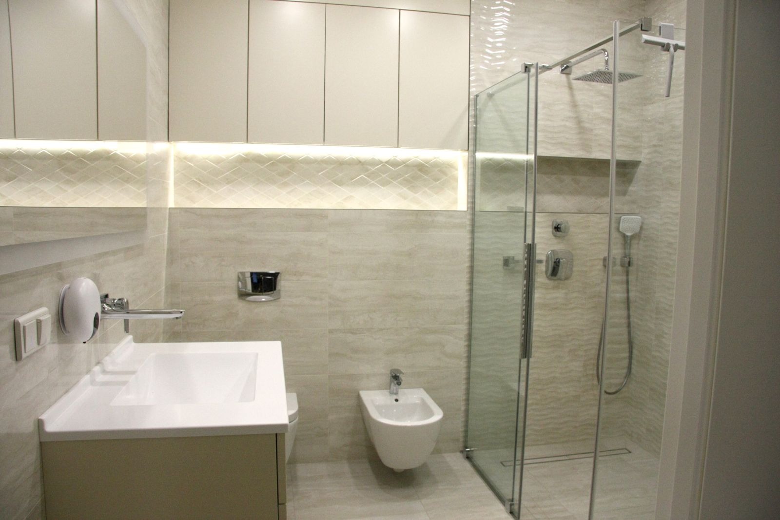 Nowoczesna łazienka w beżowych odcieniach z kabiną prysznicową typu walk-in, podświetlanym blatem z umywalką i bidetem.